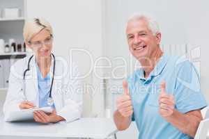 Senior patient gesturing thumbs up by doctor in clinic