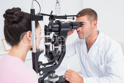Optician examining female patients eyes through slit lamp