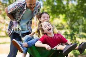 Happy father and his children playing with a wheelbarrow