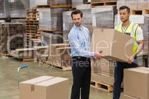 Warehouse worker and manager carrying a box together