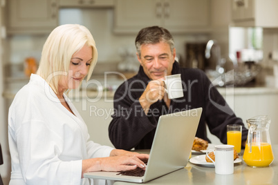 Mature couple having breakfast together woman using laptop