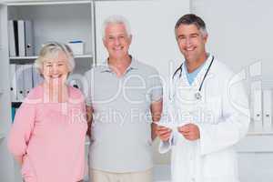 Happy senior couple with doctor standing in clinic