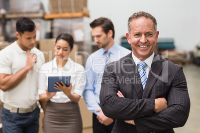 Boss standing with arms crossed in front of his employees