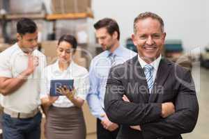 Boss standing with arms crossed in front of his employees