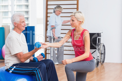 Trainer assisting senior man in exercising with dumbbells