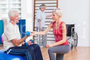 Trainer assisting senior man in exercising with dumbbells