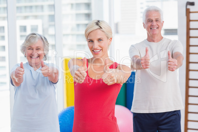 Instructor with senior couple showing thumbs up in gym