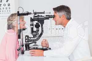 Optician examining senior patient through slit lamp