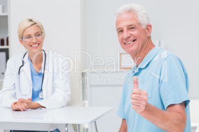 Senior patient gesturing thumbs up while doctor looking at him