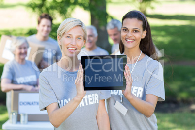 Happy volunteer friends showing tablet pc screen