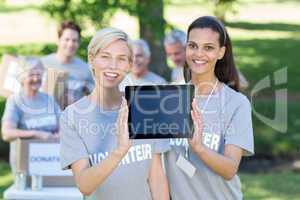 Happy volunteer friends showing tablet pc screen