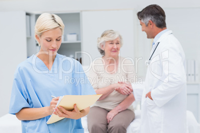 Female nurse making reports while doctor and patient shaking han