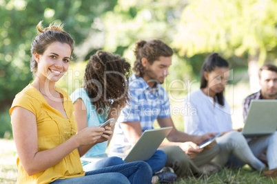 Smiling friends using media devices in park