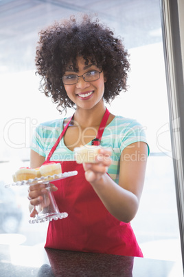 Pretty employee smiling and offering cupcake