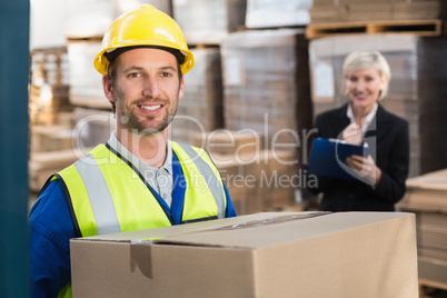 Warehouse worker holding box with manager behind him