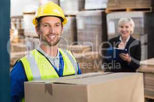 Warehouse worker holding box with manager behind him