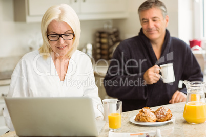 Mature couple having breakfast together woman using laptop