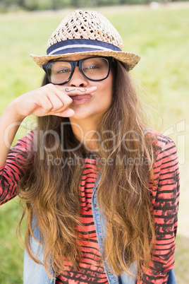 Pretty brunette in the park with mustache on finger