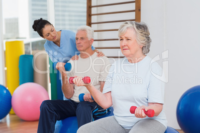 Senior woman lifting dumbbells with man and trainer at gym