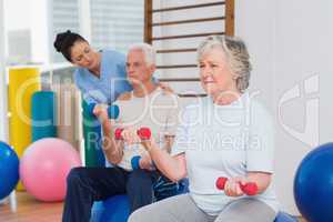 Senior woman lifting dumbbells with man and trainer at gym