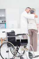 Doctor assisting senior woman to walk with wheelchair in foregro