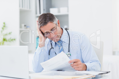 Tensed male doctor reading document in clinic