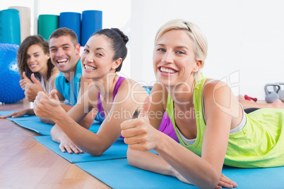 Friends gesturing thumbs up while lying on mats at gym
