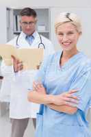 Nurse standing arms crossed while doctor reading reports in clin