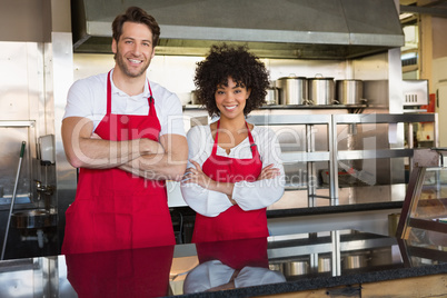 Smiling colleagues in red apron with arms crossed