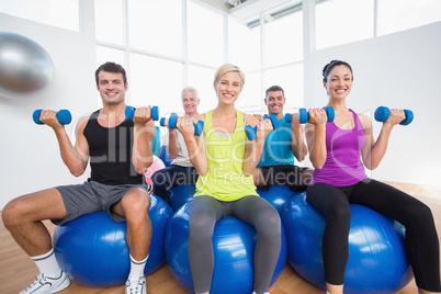People sitting on balls and lifting weights in fitness club