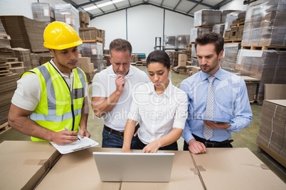 Warehouse managers and worker looking at laptop