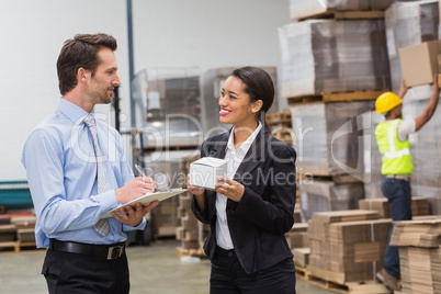 Smiling warehouse managers holding box and clipboard