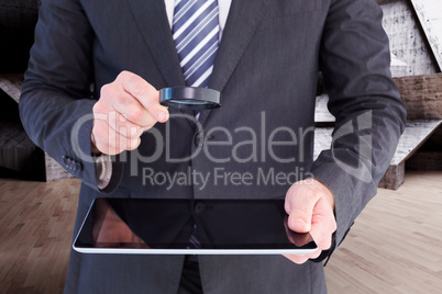 Composite image of businessman looking at tablet with magnifying