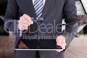 Composite image of businessman looking at tablet with magnifying