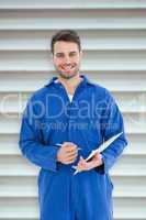 Composite image of smiling male mechanic writing on clipboard