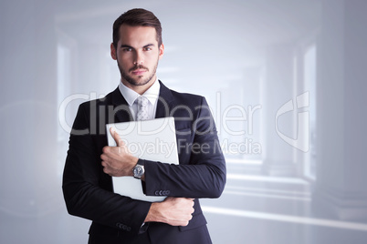 Composite image of businessman in suit posing with his laptop