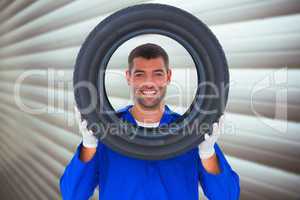 Composite image of happy mechanic looking through tire