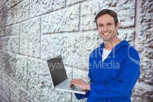 Composite image of handsome mechanic using laptop over white bac