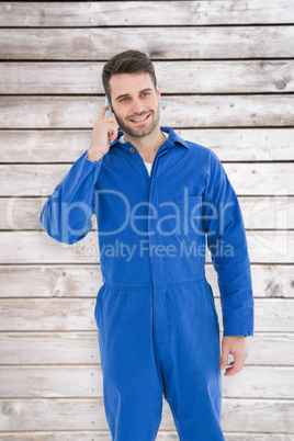 Composite image of smiling male mechanic using mobile phone