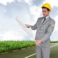 Composite image of serious architect with hard hat looking at pl