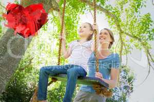 Composite image of happy mother swinging daughter at park