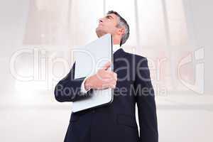 Composite image of businessman in suit holding his laptop proudl