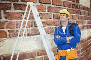 Composite image of thoughtful electrician with arms crossed by l