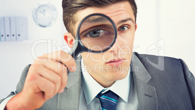 Composite image of businessman looking through magnifying glass