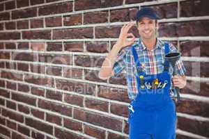 Composite image of plumber holding plunger while gesturing ok si