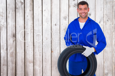 Composite image of mechanic holding tire on white background