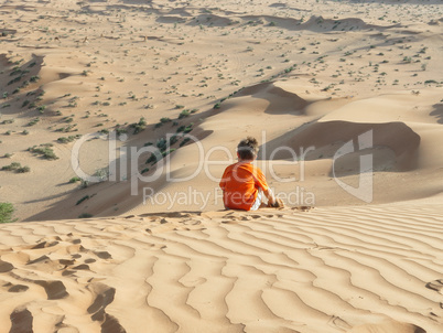 Kaukasischer Junge sitzt auf Sanddüne Rückansicht