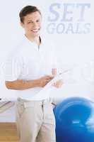 Composite image of smiling male trainer with clipboard in gym at