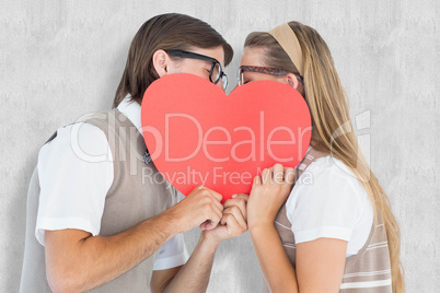 Composite image of geeky hipsters kissing behind heart card