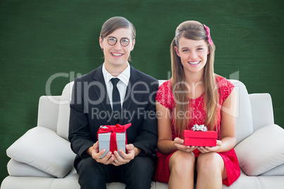 Composite image of cute geeky couple smiling and holding gift